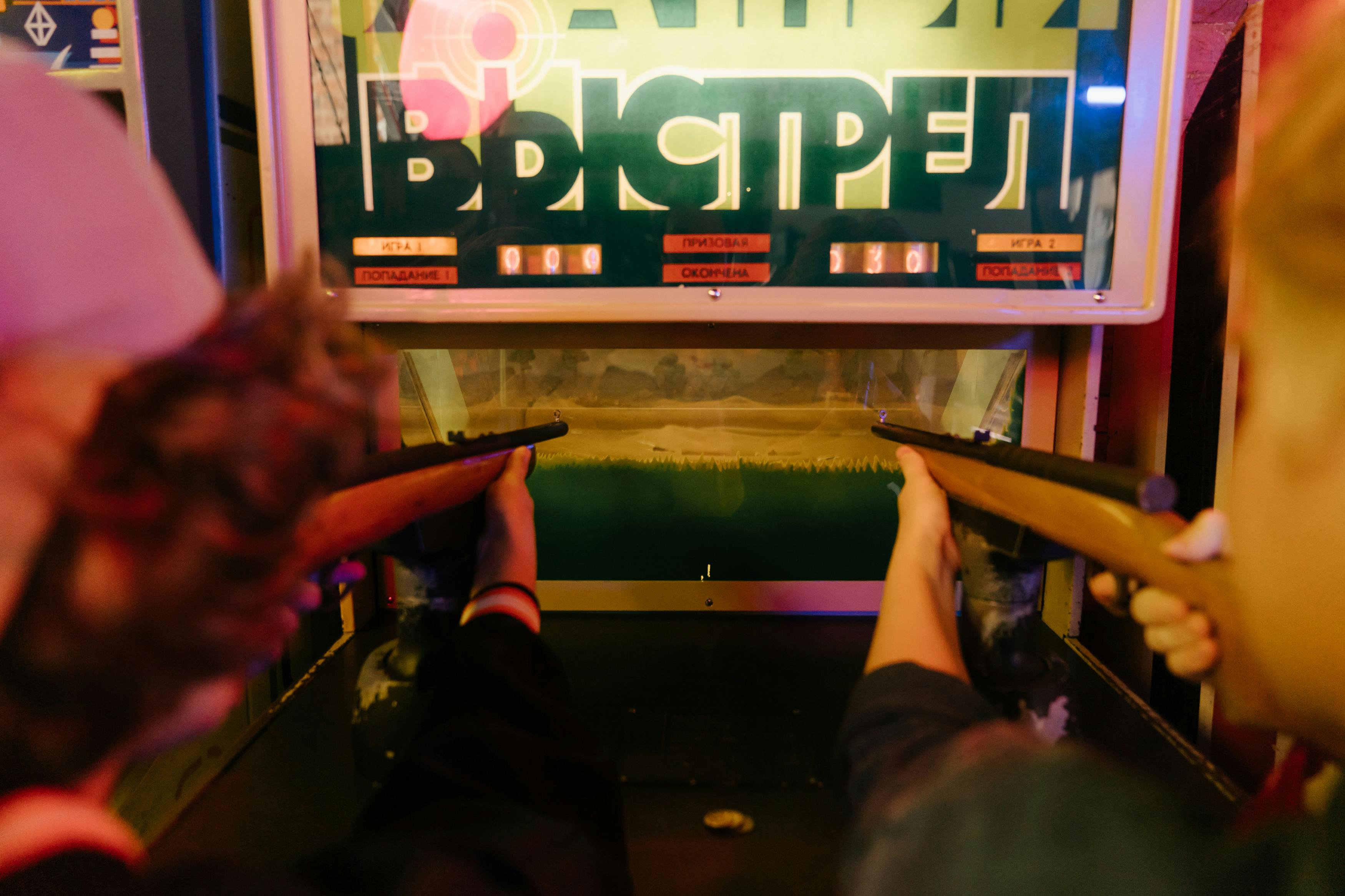 Teenagers having fun playing a vintage arcade shooting game with rifles at an amusement park arcade.
