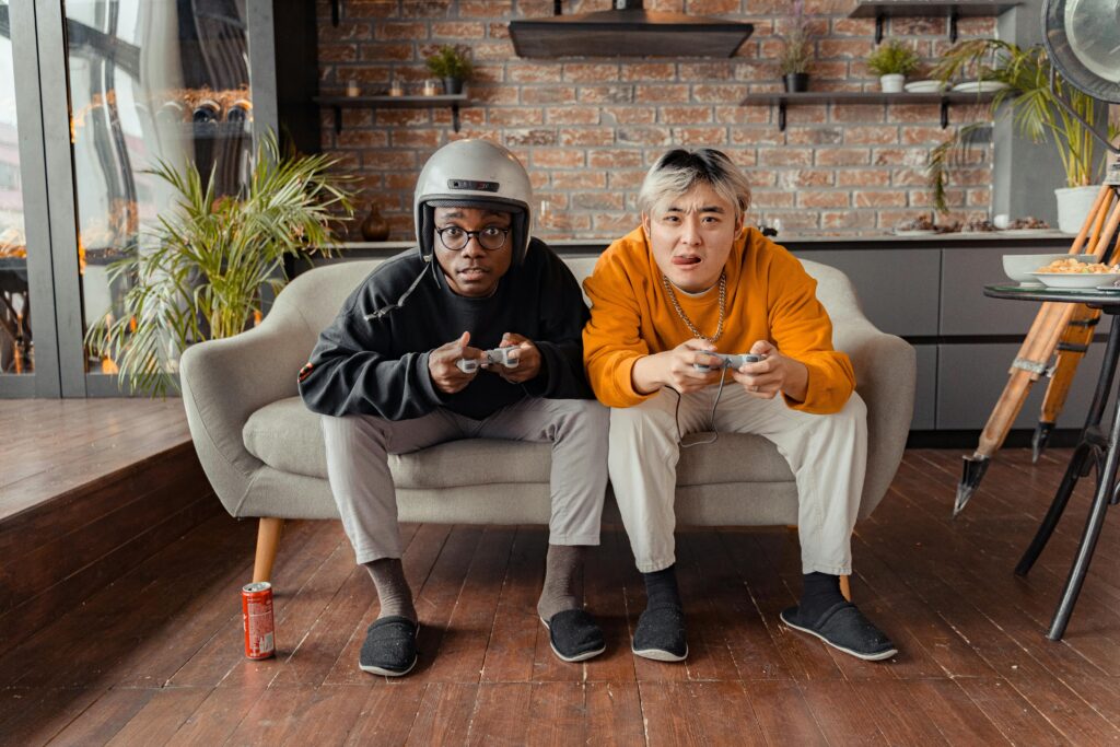 Two young men focused on video gaming indoors on a cozy sofa with controllers.