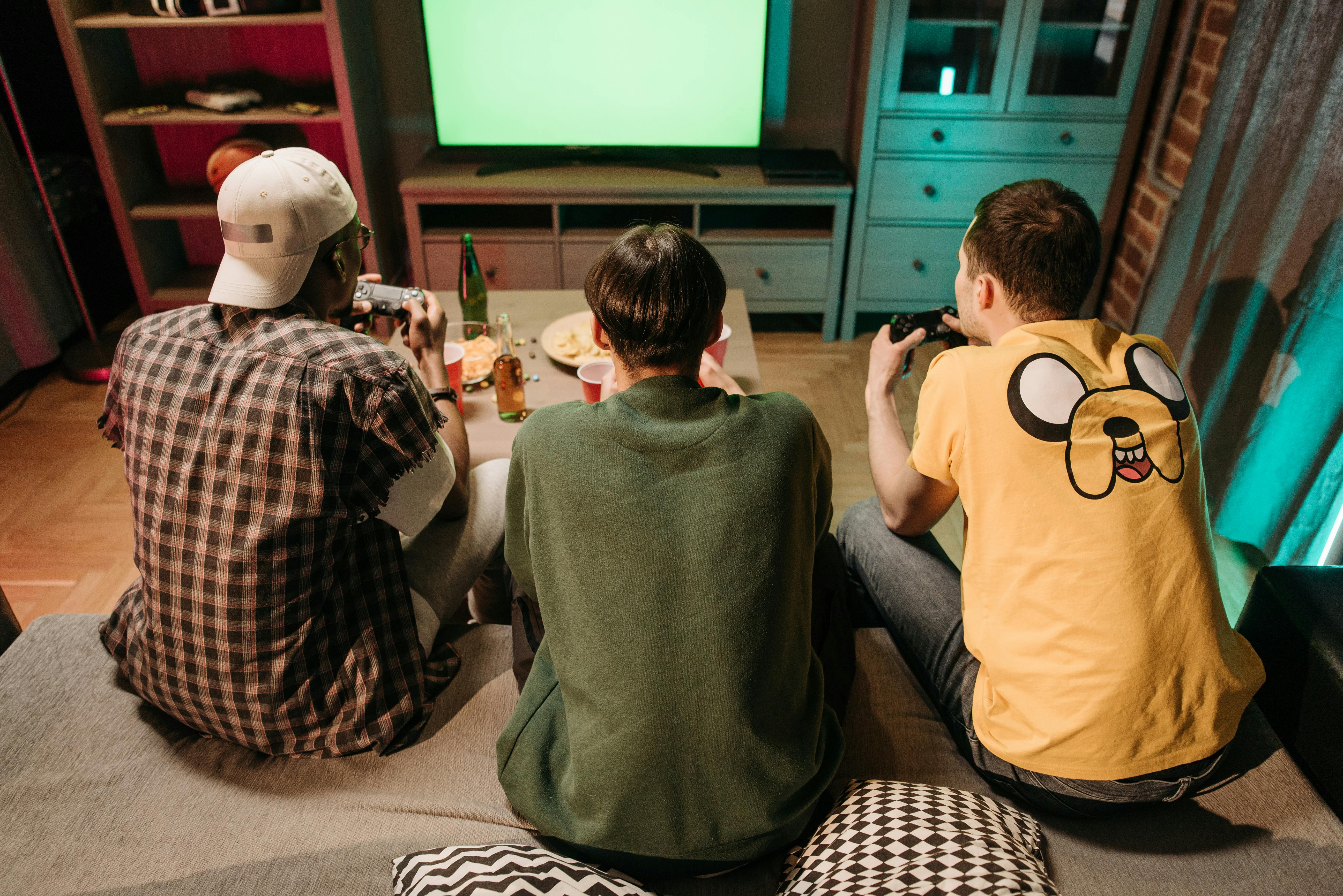 Three young men enjoying a home gaming session together, playing video games in a cozy indoors setting.